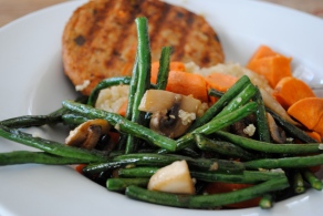 Quinoa topped with a veggie patty, sweet potatoes, and sauteed green beans and mushrooms